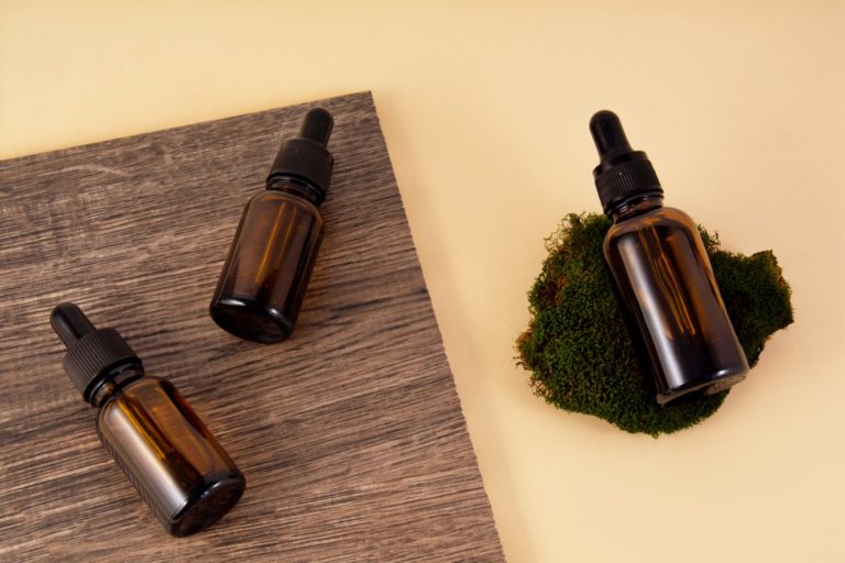 Serum bottles on ceramic tiles with wood texture and pattern on a beige background. A bottle of serum lies on the moss. Sustainable lifestyle concept, natural cosmetics. Front view